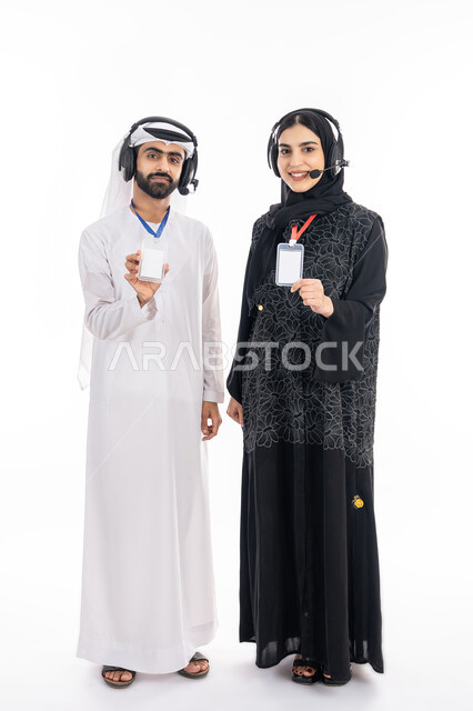 Showing personal identification, an employee identification card, a portrait of a smiling Gulf Arab and Emirati male and female employee displaying a blank white rectangular card, using headphone technology to answer customer questions and inquiries, working in the field of customer service, full body image, white background