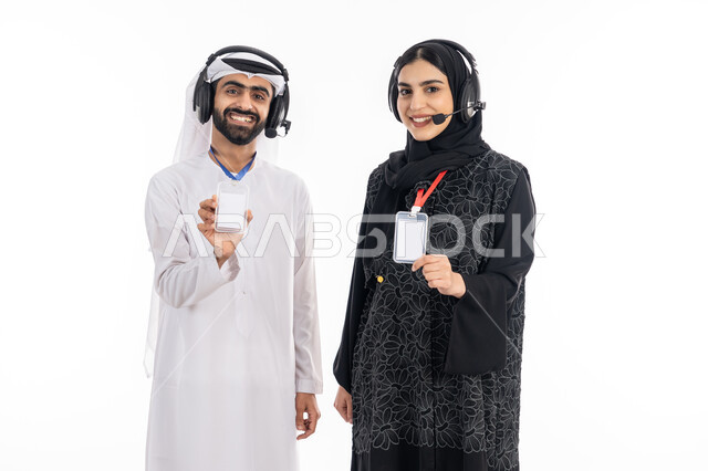 Self-expression, highlighting personal identity, employee identification card, portrait of a smiling Gulf Arab and Emirati male and female employee displaying a blank white rectangular card, using headphone technology to respond to customer questions and inquiries, working in the field of customer service, white background