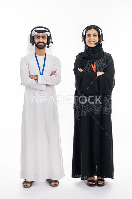 الرد على الزبائن ببشاشة وابتسامة, العمل في مجال خدمة العملاء, بورتريه لموظف وموظفة عربيين خليجين إماراتين يقفان بإيماءات أيدي متقاطعة, النظر إلى الكاميرا بتعابير الثقة بالنفس, مهن ووظائف شبابية اماراتية, تعزيز مستوى رضا العميل, صورة الجسم بالكامل, خلفية بيضاء