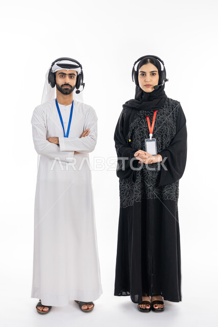 الرد على اسئلة واستفسارات الزبائن, ارتداء بطاقة تعريفية للموظفين وسماعة الاتصال, بورتريه لإمرأة عربية خليجية إماراتية ترتدي العباءة تقف بإيماءات الثقة, موظف إماراتي يعمل في مجال خدمة العملاء, تعزيز مستوى رضا العميل, صورة الجسم بالطول الكامل, خلفية بيضاء