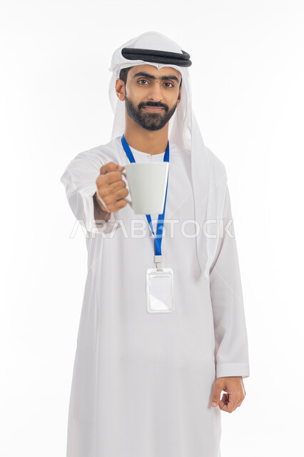 تأثير الكافيين على صحة الدماغ, المشروبات العربية التقليدية في المجتمعات الخليجية, بورتريه لموظف عربي خليجي إماراتي يرتدي الكندورة والغترة يضع البطاقة تعريفية بشريط أزرق ويحمل كوب من القهوة الساخنة, الوقوف والنظر إلى الكاميرا بابتسامة, خلفية بيضاء