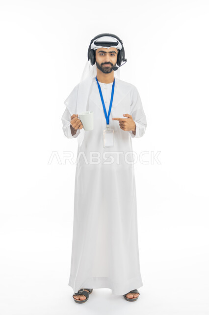 العمل في قسم الدعم الفني في الشركات الاماراتية الراقية, بورتريه لرجل عربي خليجي إماراتي يرتدي الكندورة والغترة ييضع الهديفون ويشير بيده إلى كوب من القهوة, الاجابة على اسئلة واستفسارات العملاء, صورة الجسم بالطول الكامل, خلفية بيضاء