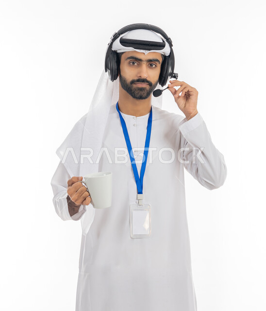 دمج التقنيات المتطورة مع العمل, التواصل مع الزبائن لحل المشكلات في مكاتب خدمة العملاء، الاجابة على الاستفسارات والاستعلامات, بورتريه لرجل عربي خليجي إماراتي يرتدي الكندورة والغترة يضع الهيدفون والبطاقة التعريفية باسم الموظف ويمسك كوب من القهوة, خلفية بيضاء