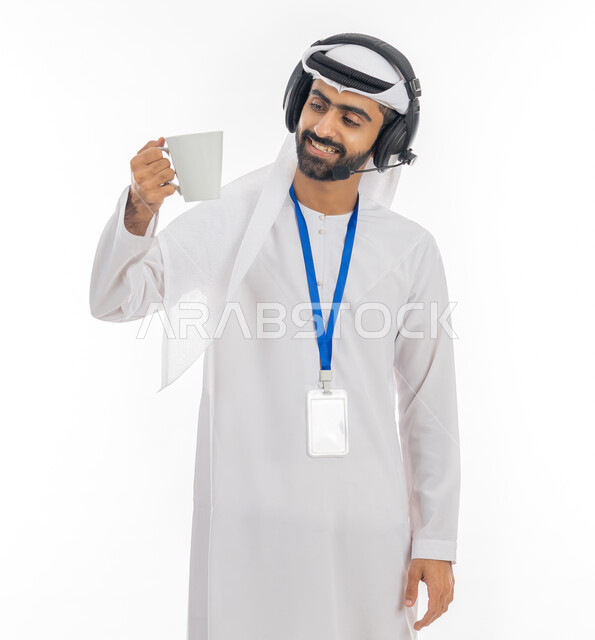 Responding to customer inquiries, working in the field of customer service and technical support, using headphone technology, enjoying hot drinks, a portrait of an Arab Gulf Emirati employee wearing a kandora and ghutra, wearing a headset and holding a cup of coffee in his hand, white background.