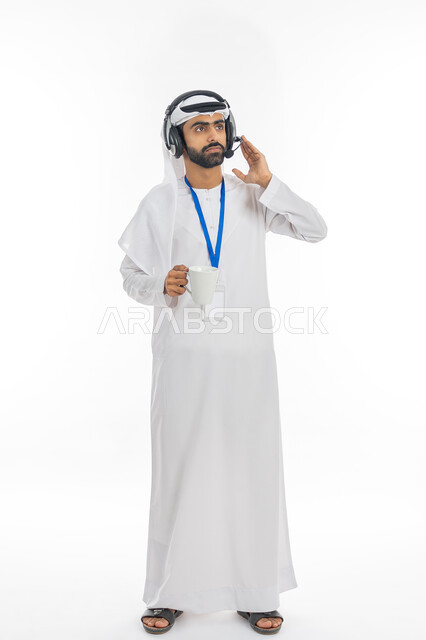 برامج التحدث عن بعد, استخدام تقنية الهيدفون، الرد والاستفسارات على الزبائن، بورتريه لرجل عربي خليجي اماراتي يرتدي الكندورة وسماعه الرأس الصوتية يمسك كوب من القهوة، مهن ووظائف إداريه اماراتية, العمل في مكاتب خدمة العملاء, صورة الجسم بالكامل,  خلفية بيضاء