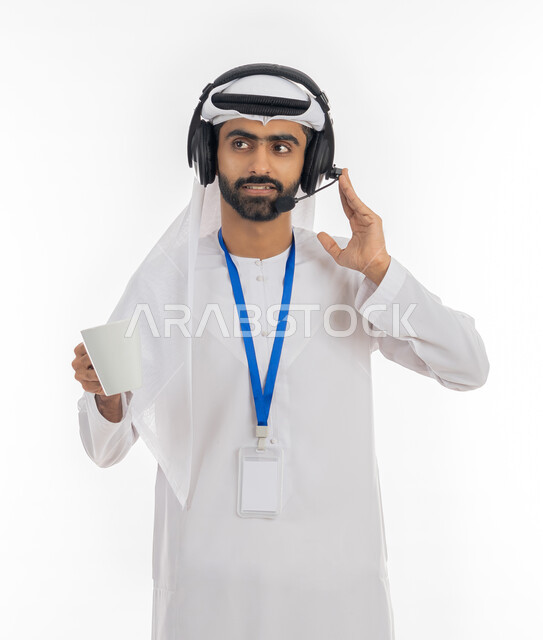الرد على الاستفسارات والتواصل مع الزبائن لحل المشكلات بإيماءات الاندماج والتركيز, استخدام سماعات الرأس والتقنيات المتطورة, بورتريه لرجل عربي خليجي إماراتي يرتدي الكندروة الاماراتية والغترة يمسك كوب من القهوة، العمل في قسم خدمة العملاء, خلفية بيضاء