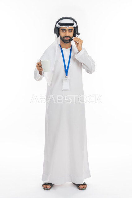 استخدام سماعات الرأس والتقنيات المتطورة, بورتريه لرجل عربي خليجي إماراتي يرتدي الكندروة الاماراتية والغترة يضع الهوية الشخصية ويمسك كوب من القهوة، العمل في قسم خدمة العملاء، التواصل مع الزبائن لحل المشكلات والرد على الاستفسارات, صورة الجسم بالكامل، خلفية بيضاء