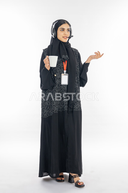 الإجابة عن الاستعلامات والاستفسارات, تعزيز مستوى رضا العميل، بورتريه لسيدة عربية خليجية اماراتية محجبة ترتدي العباءة السوداء تعمل في مجال خدمة العملاء, إمرأة سعودية تمسك كوب من القهوة وتقوم بالرد على أسئلة الزبون بتركيز, صورة الجسم بالكامل, خلفية بيضاء