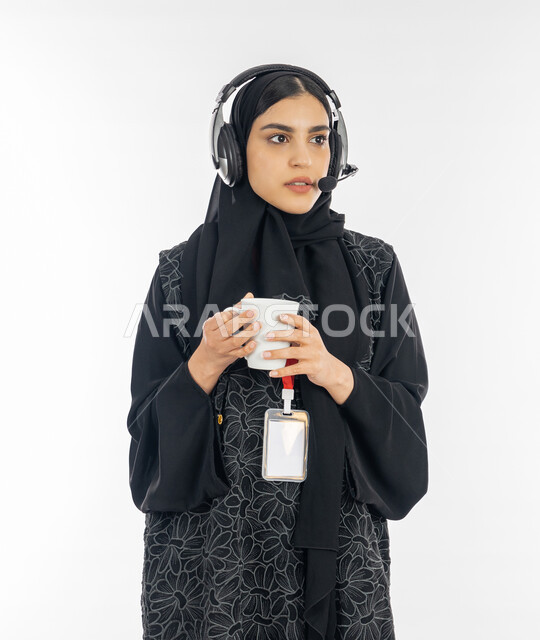 Enhancing the level of customer satisfaction, answering inquiries and inquiries, a portrait of a veiled Arab Gulf Emirati woman wearing a black abaya, wearing a personal ID and working in the field of customer service, a Saudi woman holding a cup of coffee and answering the customer’s questions with focus, white background