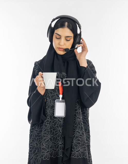 التواصل مع العملاء والاجابة على الاسئلة، بورتريه لسيدة عربية خليجية إماراتية ترتدي العباءة وسماعة الاتصال تعمل في مجال خدمة الزبائن, إمرأة سعودية تضع البطاقة التعريفية باسم الموظف وتحمل كوب من القهوة, مهن ووظائف نسائية، خلفية بيضاء