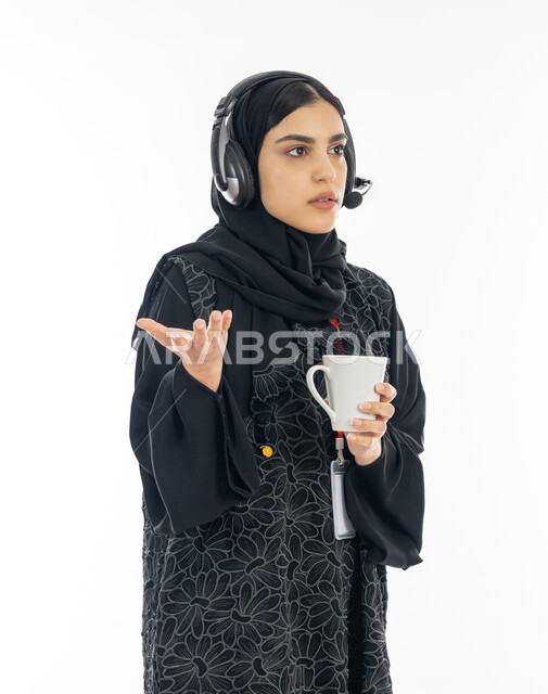 الإجابة على الأسئلة والاستفسارات بإيماءت الاستغراب, تمكين عمل المرأة في المجتمع الخليجي, بورتريه لشابة عربية خليجية اماراتية ترتدي العباءة السوداء وسماعة التواصل تعمل في خدمة العملاء, سيدة سعودية تمسك كوب من القهوة الساخنة, خلفية بيضاء
