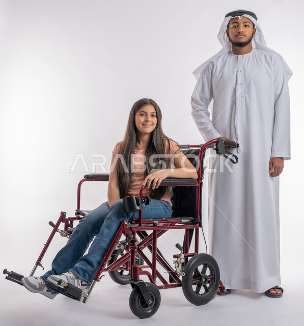تأمين أجهزة ومعدات تساعد ذوي الاحتياجات الخاصة على الحركة والتنقل, شعور المعاقين بالأمان والحنان في بيئتهم, بورتريه لفتاة عربية خليجية اماراتية ترتدي الزي الكاجوال مقعدة تجلس على كرسي متحرك تنظر إلى الكاميرا بثقة برفقة والدها, خلفية بيضاء