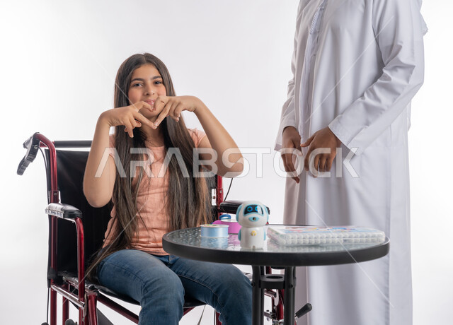 مفهوم الايجابية والدعم الأسري لذوي الهمم, تنمية المهارات والقدرات الحركية لذوي الاحتياجات الخاصة, بورتريه لفتاة عربية خليجية اماراتية مقعدة ترتدي الزي الكاجوال تجلس على كرسي متحرك ترفع يديها على شكل قلب, النظر إلى الكاميرا بإيماءات الحب والمودة, خلفية بيضاء