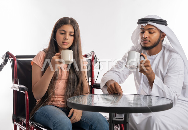 مفهوم الاهتمام بذوي الاحتياجات الخاصة, الاستمتاع بتناول المشروبات الساخنة في إحدى المقاهي الخليجية, أجواء أسرية مليئة بالعطف والحب مع أصحاب الهمم, بورتريه لفتاة عربية خليجية اماراتية مقعدة ترتدي الزي الكاجوال تجلس على كرسي متحرك برفقة والدها, خلفية بيضاء