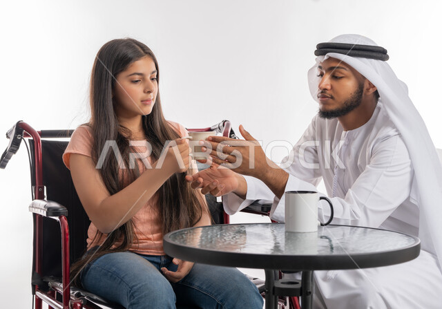 تنمية ودعم القدرة الحركية على حمل ورفع الأشياء, بورتريه لفتاة عربية خليجية اماراتية مقعدة ترتدي الزي الكاجوال تجلس على كرسي متحرك وتقوم بقضاء وقت ممتع برفقة والدها, مفهوم الاهتمام بذوي الاحتياجات الخاصة, خلفية بيضاء
