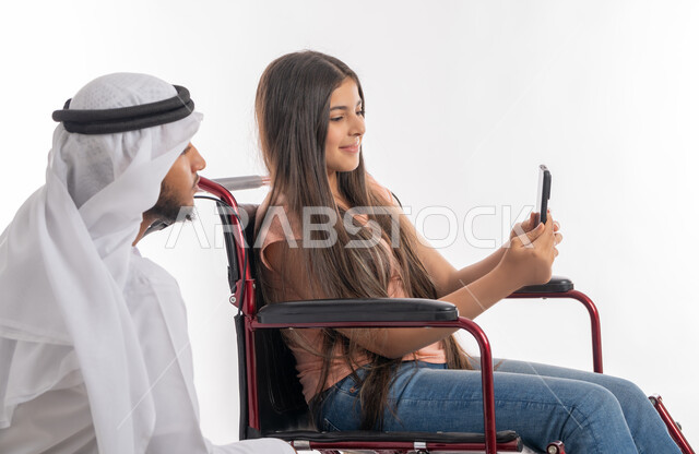 تمكين ودعم المجتمع الاماراتي لذوي الاحتياجات الخاصة, شعور المعاقين بالأمان والحنان في بيئتهم, بورتريه من الجانب لفتاة عربية خليجية إماراتية ترتدي الزي الكاجوال تقوم بالتقاط صور سيلفي تذكارية برفقة والدها عبر الهاتف المحمول, خلفية بيضاء
