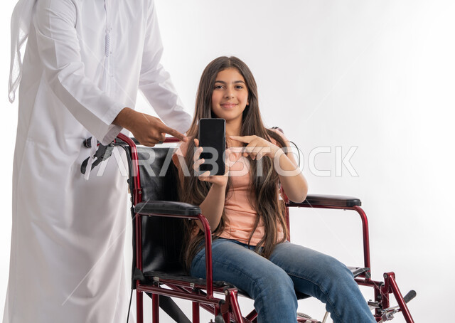تمكين المجتمع الاماراتي لذوي الاحيتاجات الخاصة, استخدام الأجهزة والتقنيات الحديثة والمتطورة, التواصل مع الأهل والأقارب عبر الجوال, بورتريه لفتاة عربية خليجية إماراتية ترتدي الزي الكاجوال تشير إلى الهاتف المحمول بشاشة سوداء فارغة برفقة والدها, خلفية بيضاء