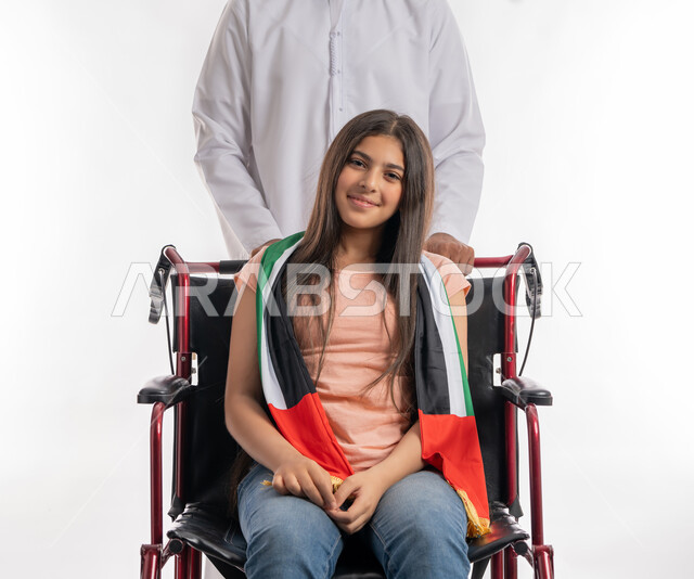 Helping people of determination to move around, celebrating with people of determination UAE Independence Day, December 2, Flag Day, November 3, portrait of an Arab Gulf Emirati girl wearing a casual outfit, sitting in a wheelchair and looking at the camera confidently and showing off her national identity, white background