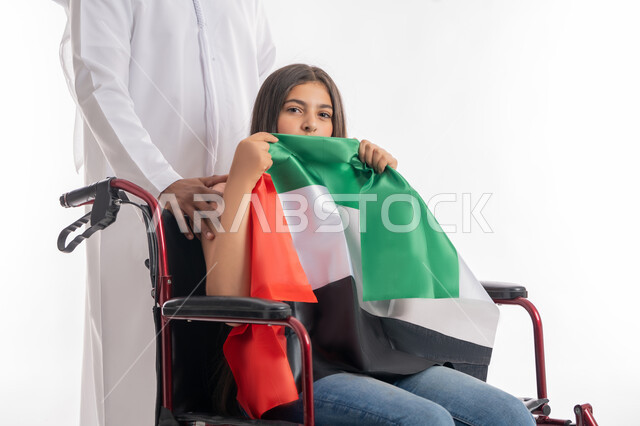 يوم العلم الاماراتي 3 نوفمير, يوم الاستقلال 2 ديسمبر, التباهي بالانتماء للوطن العربي, بورتريه لفتاة عربية خليجية إماراتية ترتدي الزي الكاجوال تجلس على كرسي متحرك وتقوم بتقبيل علم دولة الامارات بفخر واعتزاز, مساعدة ذوي الهمم على الحركة والتنقل, خلفية بيضاء