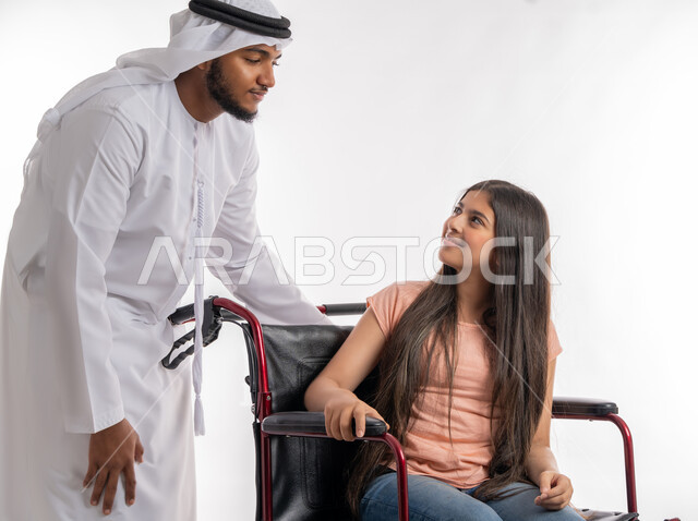 دعم المجتمع الاماراتي لذوي الاحتياجات الخاصه، تأمين احتياجات أصحاب الهمم، بورتريه لأب عربي خليجي اماراتي يرتدي الكندورة والغترة ينظر إلى ابنته بحب, نظرات مليئة بالحنان والعطف, فتاة مقعدة تجلس على كرسي متحرك، خلفية بيضاء
