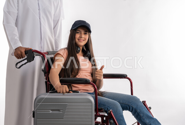 اهتمام ودعم المجتمع الإماراتي لأصحاب الهمم, الاستعداد لقضاء رحلة سياحية مع ذوي الاحتياجات الخاصة, بورتريه لفتاة عربية خليجية اماراتية مقعدة تجلس على كرسي متحرك وتمسك بيدها حقيبة السفر برفقة والدها, مساعدة ذوي الاعاقة الحركية على التنقل والحركة, خلفية بيضاء