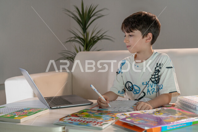 Watching educational courses to develop technical and intellectual skills, following up on online classes, an Emirati Gulf Arab boy using a laptop to solve homework, the role of technology in developing teaching methods, striving for excellence and success, integrating science with technology