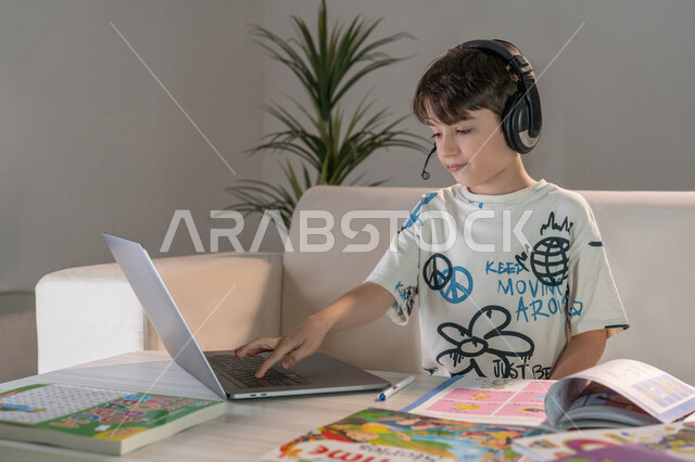 Follow up on online classes, an Emirati Gulf Arab boy uses a laptop to do homework, the role of technology in developing teaching methods, striving for excellence and success, integrating science with technology, watching educational courses to develop technical and intellectual skills
