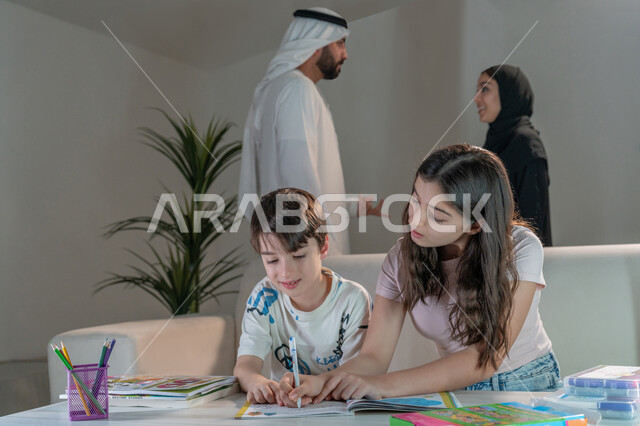 فتاة تقوم بمشاركة ومساعدة اخاها بالتلوين والانشطة الابداعية، استخدام ادوات ومعدات التلوين، رعاية وتشجيع وتطوير مهارات الابناء، قضاء اوقات عائلية ممتعة في المنزل، زوجان عربيان خليجيان إماراتيان يقومان بتبادل الآراء حول تنمية المهارات الفنية لابنائهم