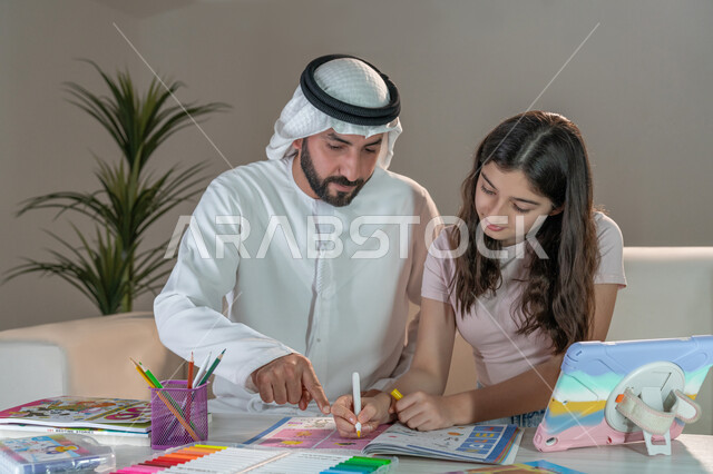 معلم خصوصي لمتابعة الدروس في المنزل، حل الواجبات المنزليه، أب عربي خليجي اماراتي يرتدي الكندورة والغترة يقوم بتعليم وتدريس ابنته، تنمية المهارات الثقافية والقدرات الفكرية للابناء