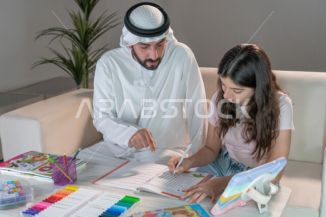 معلم خصوصي لمتابعة الدروس في المنزل، حل الواجبات المنزليه، أب عربي خليجي اماراتي يرتدي الكندورة والغترة يقوم بتعليم وتدريس ابنته، تنمية المهارات الثقافية والقدرات الفكرية للابناء