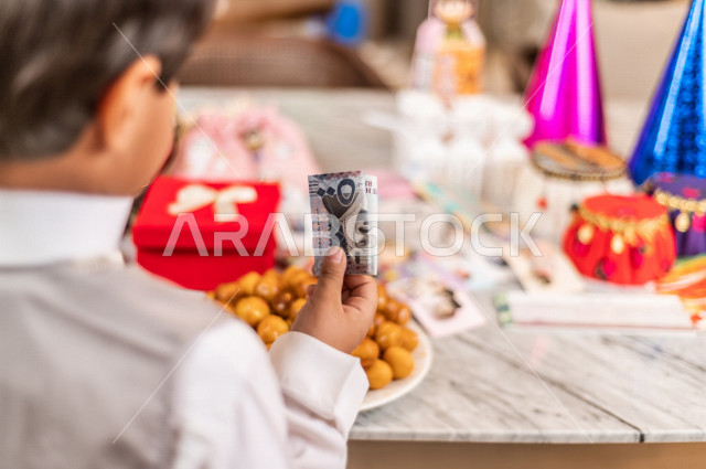 طفل سعودي خليجي سعيد ، يرتدي لباس العيد الانيق ، يأخذ العيدية  ، الاحتفال بعيد الفطر السعيد ، عيد الفطر المبارك  ،  تقديم العيديات و الحلوى ، القرقيعان