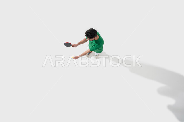 ممارسة رياضات وانشطة بدنية شبابية ممتعة، التركيز باللعب واتقانه، بورتريه للاعب عربي خليجي سعودي يرتدي ملابس رياضية يحمل بيده مضرب وكرة تنس الطاولة، المحافظة على الرياضة والرشاقة الجسدية، خلفية بيضاء