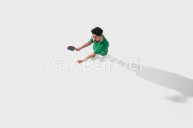 مفهوم التركيز وسرعة البديهة، ممارسة رياضات وانشطة بدنية شبابية، بورتريه للاعب عربي خليجي سعودي يرتدي ملابس رياضية يحمل بيده مضرب وكرة تنس الطاولة، المحافظة على الرياضة والرشاقة الجسدية، التسلية بالفعاليات الصيفية الممتعة, احتراف وإتقان لعبة البادل, خلفية بيضاء
