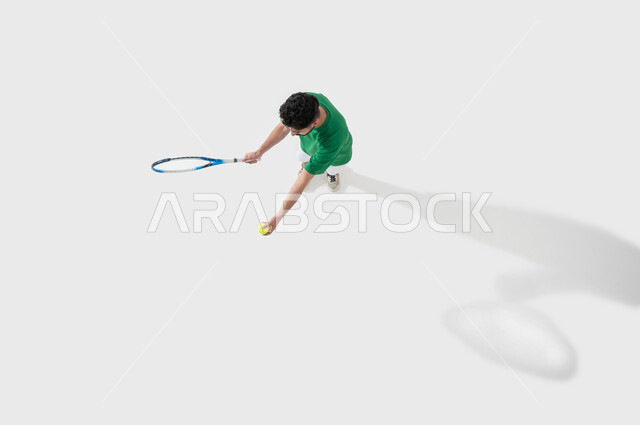 Performing racquet sports exercises, playing with speed and concentration, a portrait of a young Saudi Arabian Gulf man wearing sports clothes and holding a tennis racket in his hand, practicing sports and fun physical activities, expressions and gestures that indicate enthusiasm and engagement with exercise, maintaining health and physical fitness, white background