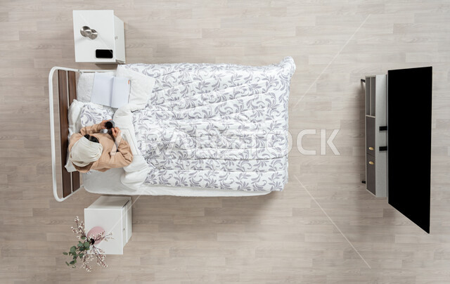 الاستمتاع بالمشروبات الساخنه على السرير بورتريه عامودي علوي لإمرأة عربية خليجية سعودية محجبه تجلس في سريرها مستلقيه تحت لحافها تحمل بيدها كوب القهوة، الاكل والشرب في غرفه النوم، خلفيه بيج