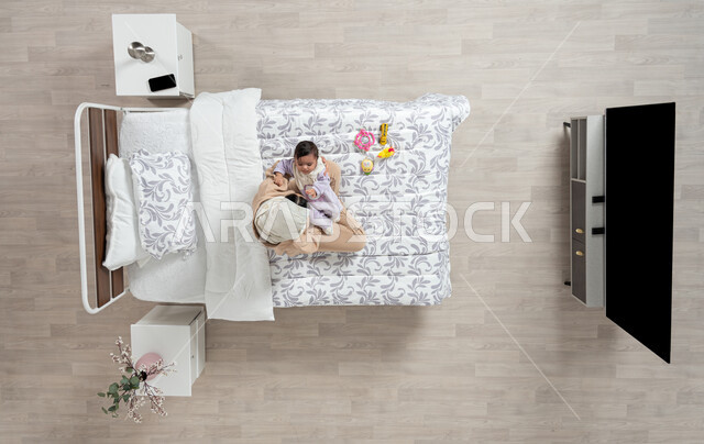 النظر إلى الاطفال بإيماءات الحب والحنان، مداعبه الام لاطفالها الصغار، بورتريه عامودي علوي لأم عربيه خليجيه سعوديه  محجبة تحمل وتداعب ابنتها حديثه الولاده على سريرها, رضيعه ترتدي بربتوز قطني ناعم, الرعاية والاهتمام بالأبناء, خلفيه بيج