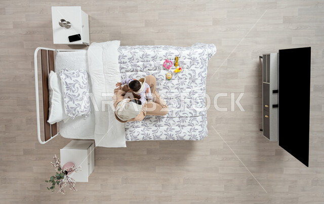 النظر إلى الاطفال بإيماءات الحب والحنان، مداعبه الام لاطفالها الصغار، بورتريه عامودي علوي لأم عربيه خليجيه سعوديه  محجبة تحمل وتداعب ابنتها حديثه الولاده على سريرها, رضيعه ترتدي بربتوز قطني ناعم, الرعاية والاهتمام بالأبناء, خلفيه بيج