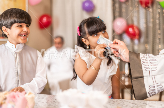 طفلة سعودية خليجية سعيدة ترتدي لباس العيد الانيق ، تأخذ العيدية  ، الاحتفال بعيد الفطر السعيد ، عيد الفطر المبارك  ،  تقديم العيديات و الحلوى ، القرقيعان