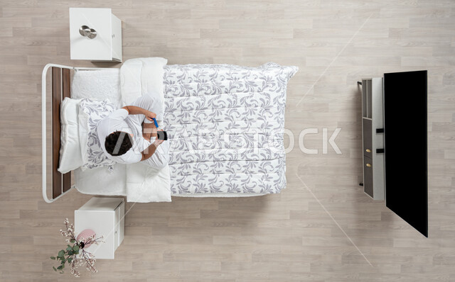 Quick purchase with a bank card, a portrait of a Saudi Arabian Gulf man wearing a flannel and white underpants, sitting on his bed, holding a mobile phone and bank credit card in his hand, purchasing and paying through mobile programs and applications, paying bills online, beige background