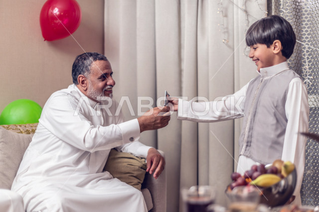 طفل سعودي خليجي سعيد ، يرتدي لباس العيد الانيق ، يأخذ العيدية  ، الاحتفال بعيد الفطر السعيد ، عيد الفطر المبارك  ،  تقديم العيديات و الحلوى ، القرقيعان