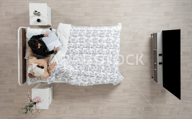 الاهتمام بتربيه ورعايه الابناء، بورتريه عمودي علوي لسيده عربيه خليجيه سعوديه تجلس على سريرها وتقوم بتدريس ابنها البالغ الذي يحمل كتابا للقراءه والمطالعه، اهميه التدريس والتعليم، المذاكره والحفظ، خلفيه بيج