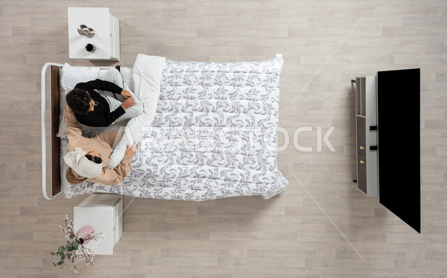 الاهتمام بتربيه ورعايه الابناء، بورتريه عمودي علوي لسيده عربيه خليجيه سعوديه تجلس على سريرها وتقوم بالتحدث مع ابنها البالغ برفق وهدوء، حب وحنان الاهل، خلفيه بيج