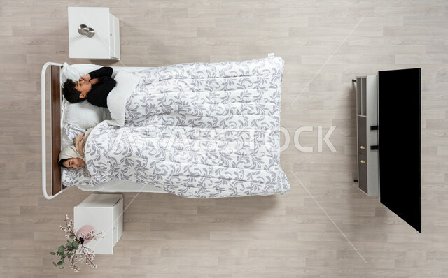 النوم بعمق من الارهاق والتعب، بورتريه عمودي علوي لسيده عربيه خليجيه سعوديه محجبه مستلقيه على سريرها بجوار ابنها، اخذ قيلولة و قسط من الراحة، الكسل والخمول والحاجة الى النوم، خلفيه بيج