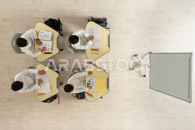 آفاق و مهارات التعليم، انشطة ترفيهية ممتعة، بورتريه علوي عامودي لتلاميذ عرب خليجيون سعوديون يرتدون الثوب السعودي التقليدي يجلسون على الكراسي وأمامهم طاولات الدراسة، قرطاسية و أدوات مدرسية، الترفيه وقضاء اوقات مسلية من خلال الرسم والتلوين، خلفية بيج