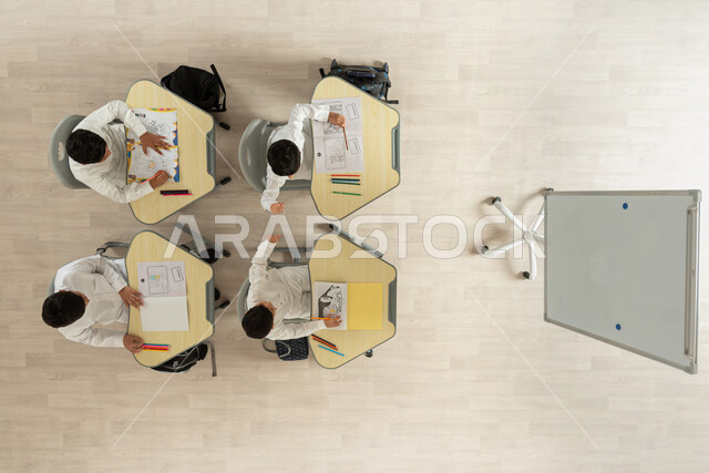 الترفيه وقضاء اوقات مسلية من خلال الرسم والتلوين، بورتريه علوي عامودي لتلاميذ عرب خليجيون سعوديون يرتدون الثوب السعودي التقليدي يجلسون على الكراسي وأمامهم طاولات الدراسة، انشطة ترفيهية ممتعة، خلفية بيج