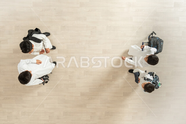 الألفة والانسجام والمودة، الانتهاء من يوم دراسي مثمر، مغادرة قاعة الدراسة بعد انهاء الواجبات المدرسية، بورتريه علوي عامودي لمجموعة أولاد عربيين خليجيين سعوديين يرتدون الثوب التقليدي و يحملون حقائبهم، خلفية بيج