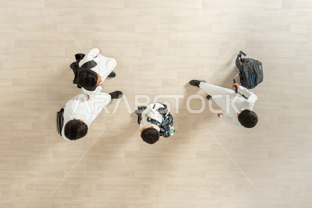 الانتهاء من يوم دراسي مثمر، مغادرة قاعة الدراسة بعد انهاء الواجبات المدرسية، بورتريه علوي عامودي لمجموعة أولاد عربيين خليجيين سعوديين يرتدون الثوب التقليدي و يحملون حقائبهم، خلفية بيج