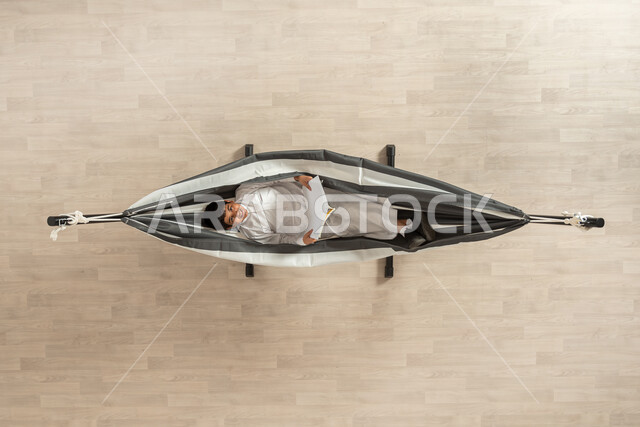 تمضية أوقات الفراغ بالتعلم والتثقيف الذاتي،بورتربه علوي عامودي لرجل عربي خليجي سعودي مبتسم يرتدي الثوب التقليدي يحمل بيده كتاب، قضاء أوقات هادئة في المنزل، قراءة الروايات والقصص، ايماءات التركيز والاستمتاع، ممارسة هواية المطالعة