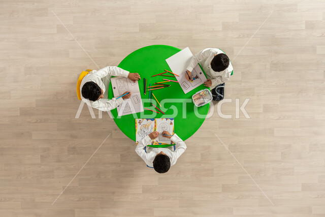 Entertaining and artistic activities for students, developing skills, education and creativity, drawing techniques for the pre-school stage, a vertical overhead portrait of students from the Kingdom of Saudi Arabia doing a drawing coloring activity, beige background