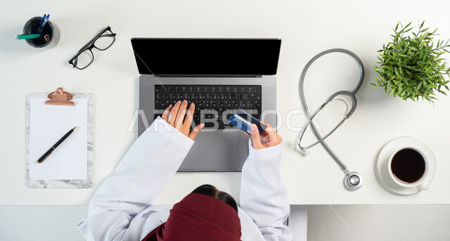 التسويق للأدوات الحديثة، الخدمات والأجهزة الطبية، مفهوم الطب والرعاية الصحية، بورتريه علوي عامودي لإمرأة عربية خليجية سعودية ترتدي المعطف الطبي تستخدم الحاسوب المحمول، الدفع عن طريق بطاقة المصرف البنكية، دمج التكنولوجيا بالحياة اليومية، خلفية بيضاء